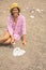 Happy travel woman in yellow hat arrangement sea pebble heart shape sitting on sunny sand beach