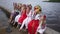 Happy Ukrainian women looking up at cloudy sky smiling talking sitting on river pier outdoors. Wide shot group of