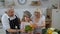 Happy vegan senior couple dancing with granddaughter child while cooking vegetables in kitchen