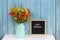 Happy Wednesday words on black letter board and bouquet of bright wildflowers in tin can vase on table against blue wooden wall.