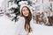 Happy winter moments of joyful young woman with long brunette hair, white winter clothes having fun on street in snowing