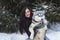 Happy winter time of joyful young woman playing with cute husky dog in snow on street.