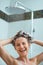 Happy woman applying shampoo in shower