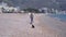 Happy woman with backpack AND sunglasses walks with playful Dachshund dogs along sand beach against resort hotels on