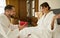 Happy woman in bathrobe sitting on bed after waking up pleasantly surprised by her loving partner presenting her with a red gift