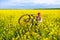 Happy woman with a bicycle in a rapeseed field, during a countryside bike tour in rural parts of Romania, Eastern Europe.