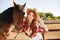 Happy woman cowgirl standing with horse and showing peace sign