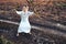 Happy woman in a dress dances barefoot on a muddy field, holding reeds in her hands