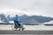 A happy woman dressed in a blue coat sits in a wheelchair on a point view and looking at the snow-capped mountains.