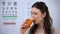 Happy woman drinking healthy fresh carrot juice, eyechart on background, vision