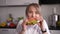 Happy woman eating burger with pleasure in kitchen