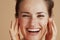 Happy woman with face scrub against beige background