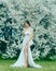 Happy woman fashion model standing, white evening dress silhouette mermaid. Slit sexy bare leg. girl bride perfect gown