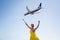 Happy woman with hands up on a blue sky background with real airplane flying over her head