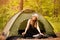 Happy woman in hat sits in tent around forest enjoying leisure and freedom