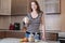 Happy woman holding a glass of organic oat milk in the kitchen. Bottle and fruit on the table. Diet vegetarian product