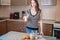 Happy woman holding a glass of organic oat milk in the kitchen. Bottle and fruit on the table. Diet vegetarian product