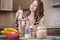 Happy woman holding a glass of organic oat milk in the kitchen. Bottle and fruit on the table. Diet vegetarian product