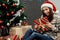 happy woman holding surprised christmas present box. girl in sweater with deers and wearing santa hat in festive room with lights