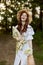 a happy woman in a light summer dress stands in nature with a wicker hat, a plaid and a basket with daisies