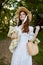 a happy woman in a light summer dress stands in nature with a wicker hat, a plaid and a basket with daisies