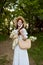 a happy woman in a light summer dress stands in nature with a wicker hat, a plaid and a basket with daisies