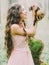 The happy woman with long curly hair in the light pink dress holding, petting and playing with the ferret in the green