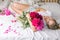 Happy woman lying on the bed wearing pajamas, enjoying tulip flowers bouquet of peony