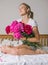 Happy woman lying on the bed wearing pajamas, enjoying tulip flowers bouquet of peony