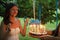 happy woman making a wish and blowing candles on cake at her bridal shower in summer park, joyful moment at party or birthday