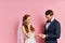 Happy woman and man wearing tux and white wedding dress isolated over pink ackground