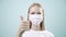 Happy woman in medical mask look and show thumb up, cool, to the camera on light background. Health protection Corona Virus concep