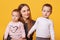 Happy woman, mother and her twin toddlers poses in photo studio isoleted over yellow background. Mommy looks at her infants with