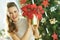 Happy woman near Christmas tree showing red poinsettia