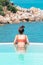 Happy woman in orange swimsuit swimming in infinity pool at luxury hotel against ocean front. young female enjoy in tropical