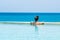 Happy woman in orange swimsuit swimming in infinity pool at luxury hotel against ocean front. young female enjoy in tropical