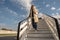 Happy woman passenger in sunglasses going down on aircraft stairs after landing at airport