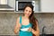 A happy woman with a plate and spoon in her hand is eating standing in the kitchen.