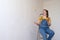 Happy woman playing with brush on ladder in a room with an unpainted wall with copy space. Independent single female