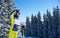 Happy woman posing on skis before skiing. Sunny day at ski resort. Clear blue sky, snow-covered fir trees on background.