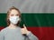 Happy woman in protective mask holding thoumb up on national flag Bulgaria background. Flu epidemic and virus protection concept