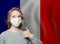 Happy woman in protective mask holding thumb up on national flag France background. Flu epidemic and virus protection concept