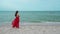 Happy woman in red dress standing with arms crossed on sea beach with wind blow