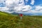 Happy woman in a red jacket, with hands up against a background of beautiful mountains and a beautiful cloudy sky. Leisure. Hiking