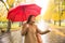 Happy woman with red umbrella walking at the rain in beautiful autumn park