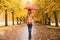 Happy woman with red umbrella walking at the rain in beautiful autumn park