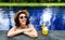 Happy woman relaxing in the swimming pool during summer vacation in tropical resort. Female on holidays drinks juice.