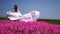 Happy Woman run in the park among lush pink flowers, slow-motion. Girl in white flying dress with long hair in the