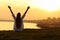 Happy woman seeing city at sunset and raising arms