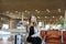 Happy woman sitting in airport hall with modern tablet near valise and showing thumbs up.